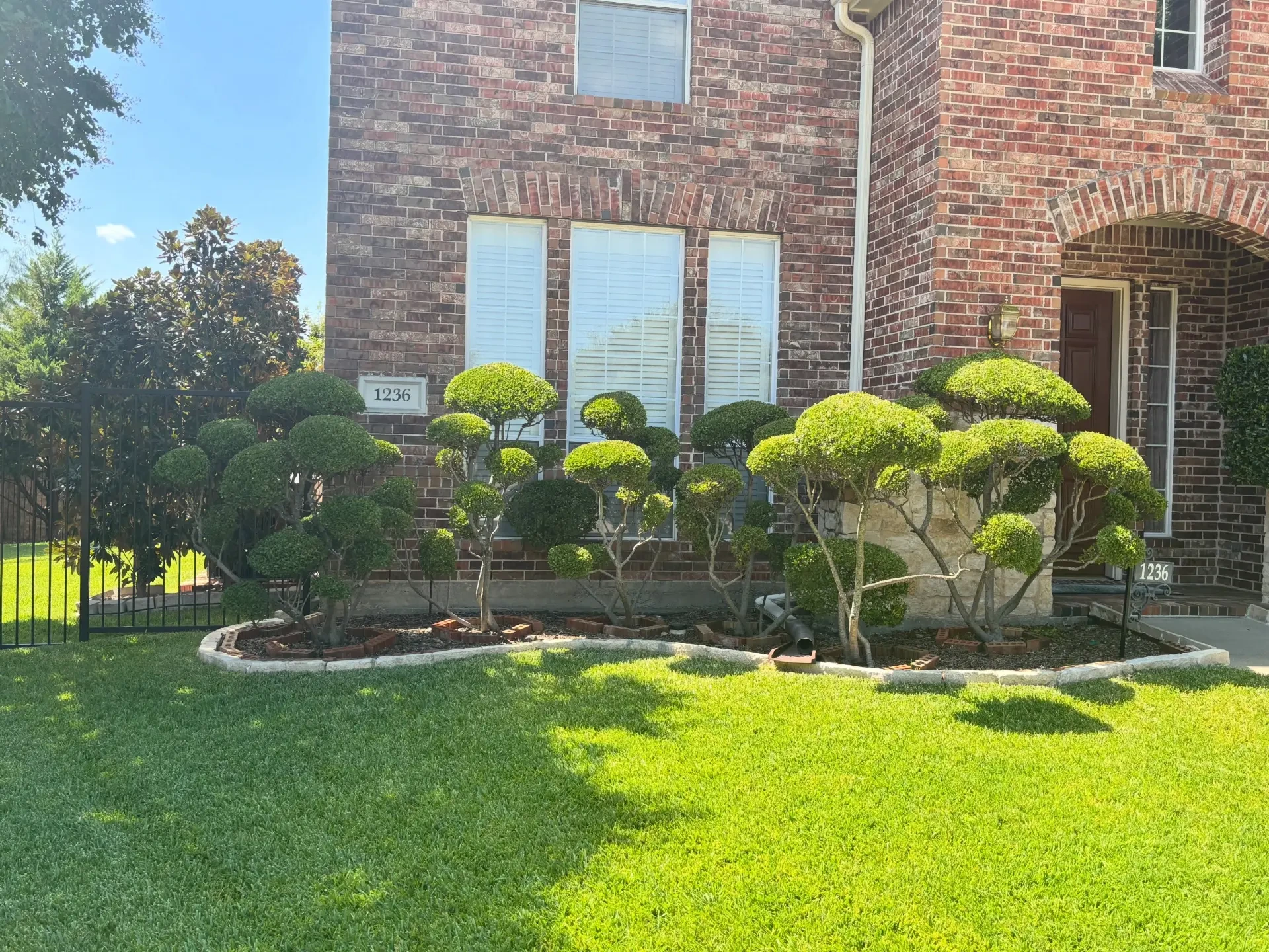 Gibbys Exterior landscape work with manicured shrubs and a lush lawn in front of a brick home